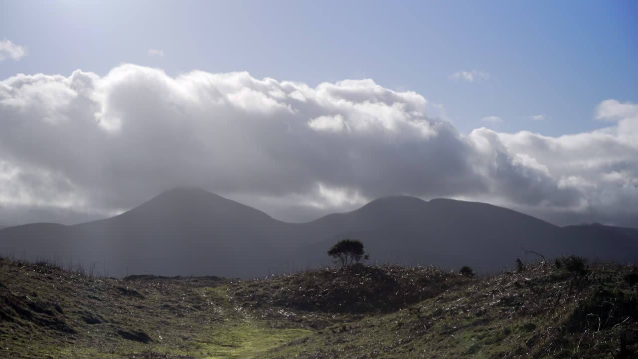 cordillera irlandesa con nubes turbulentas, rayos de sol y arbustos solitarios, ideal para caminar de vacaciones