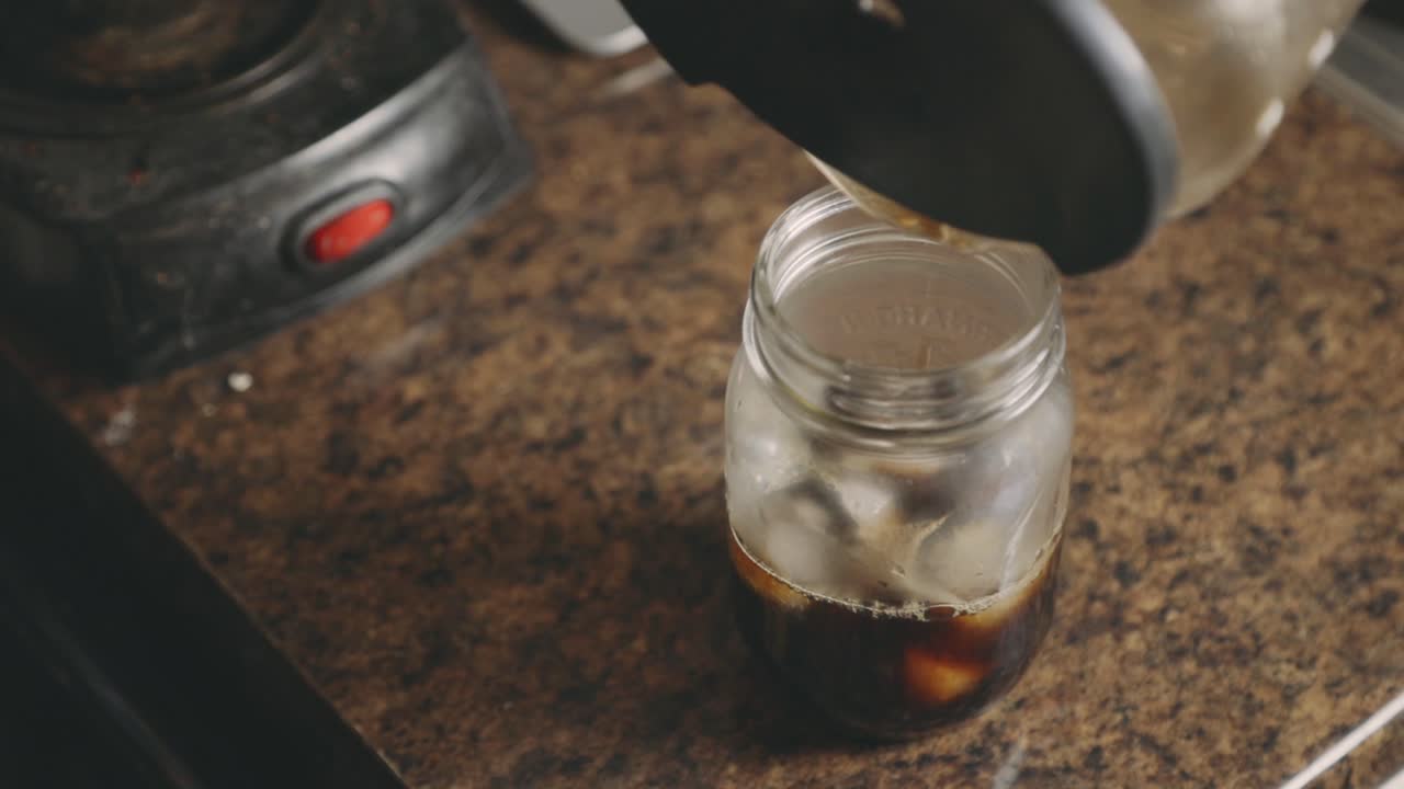 verter a mano café negro de una cafetera a un vaso con hielo - disparo en ángulo alto