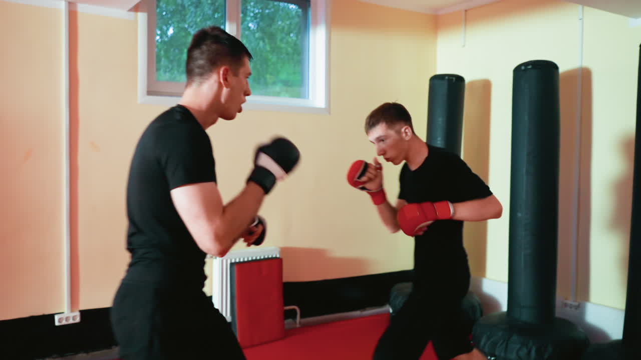 Boxers sparring session inside gym with red padded floor, standing face to face throwing punches stance, wearing gloves, focused on movement, during combat training