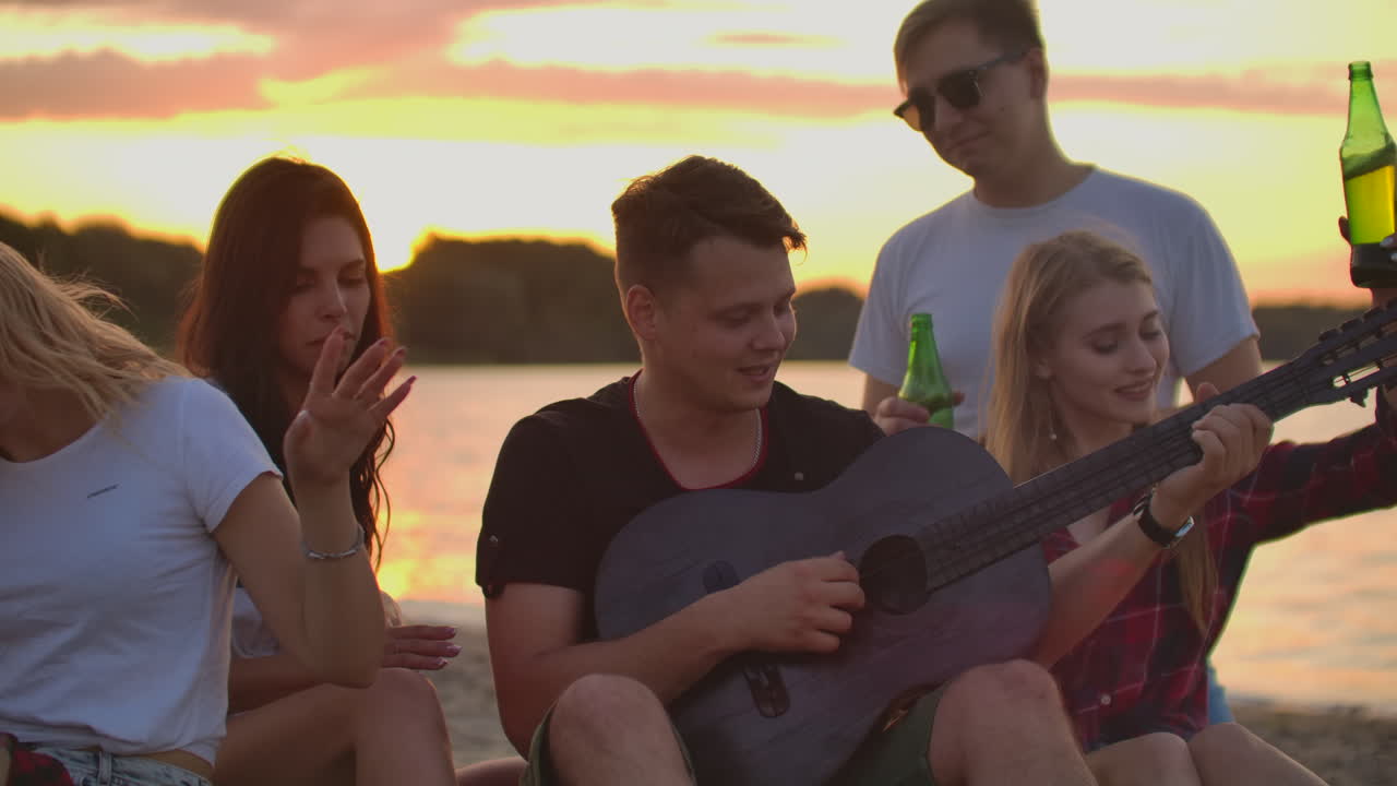 Gli amici suonano la chitarra e cantano canzoni intorno a un falò a una festa in spiaggia. Questa è un'emozionante serata estiva con i migliori amici e birra.