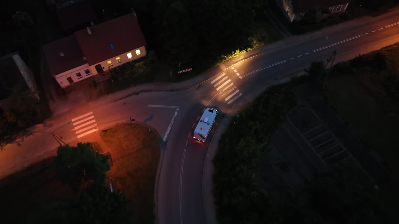 High angle drone shot a camper van driving through a illuminated town, night