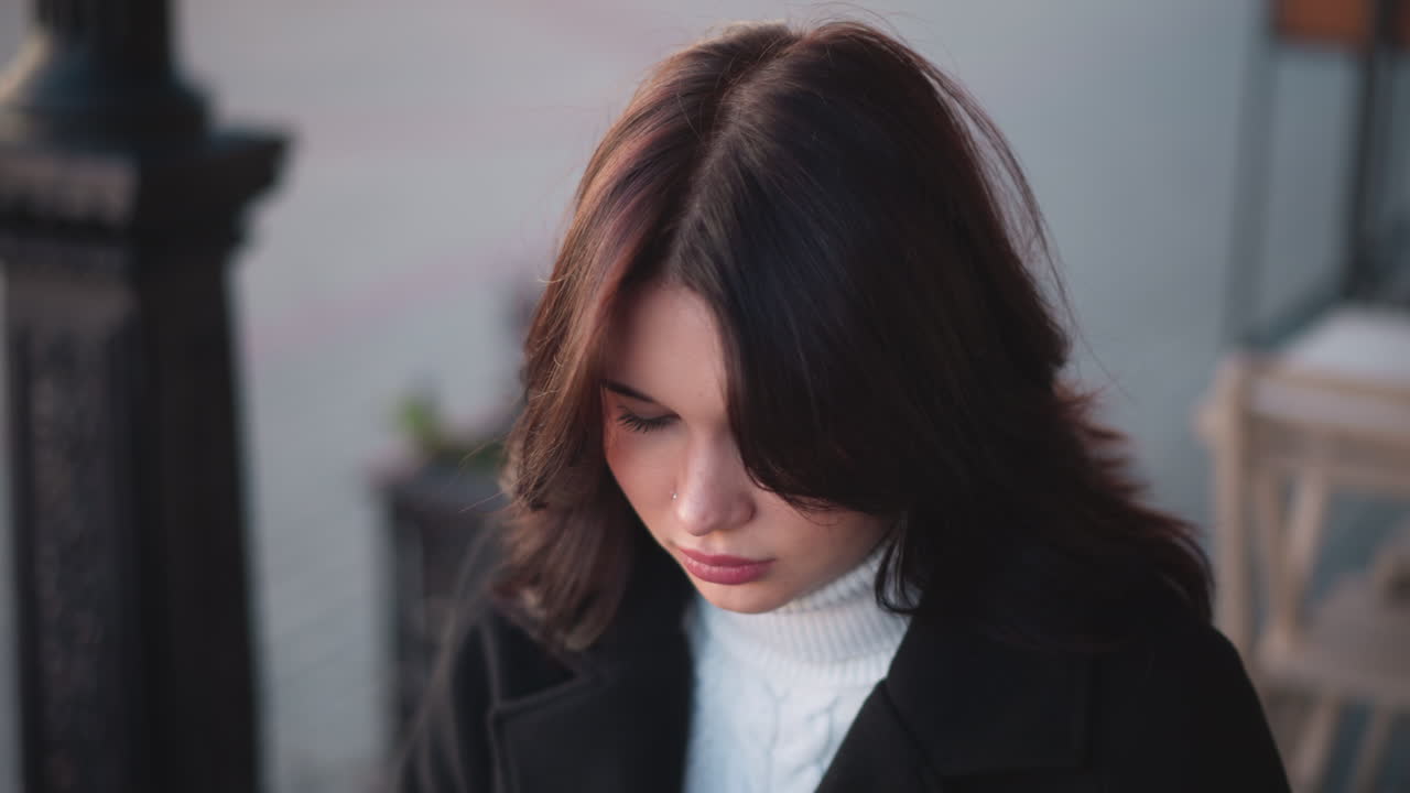 야외에서 앉아있는 사려 깊은 젊은 여성은 색 터틀과 검은색 코트를 입고, 부드러운 갈색 머리카락이 얼굴을 틀고, 평온하고 내면적인 분위기를 만니다.