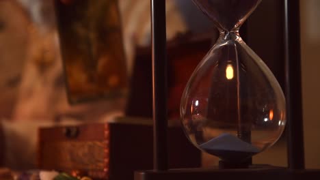 hourglass marking the time with its blue sand, with a man taking tarot cards one by one from a small coffer near some stones in the background