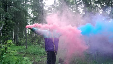 man releasing pink and blue smoke bombs in a forest