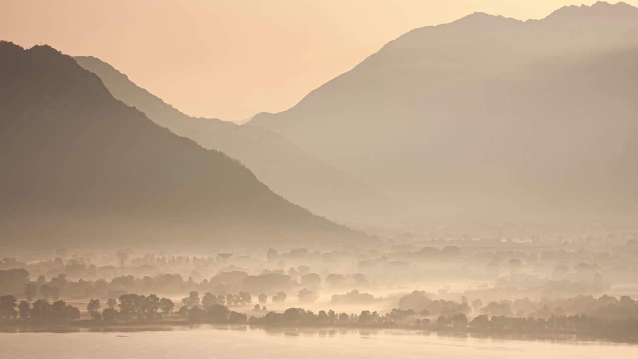 A wide timelapse shot of a foggy morning near Lake Como, featuring rolling hills in the background. The tranquil atmosphere is beautifully captured in soft light.