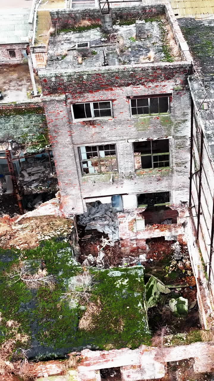 Debris and construction garbage inside and outside the broken factory buildings. Ruined plant exterior from aerial perspective. Vertical video