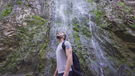 young man turns around in front of the waterfall.