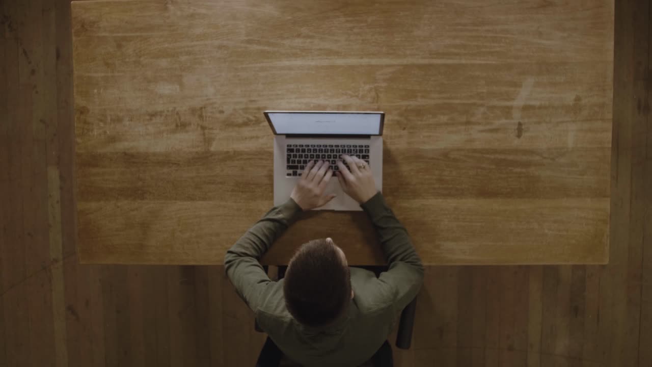 A Guy Using His Laptop Computer For His Work On A Wooden Table - Top View Shot