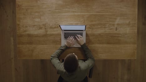 un tipo que usa su computadora portátil para su trabajo en una mesa de madera - vista superior