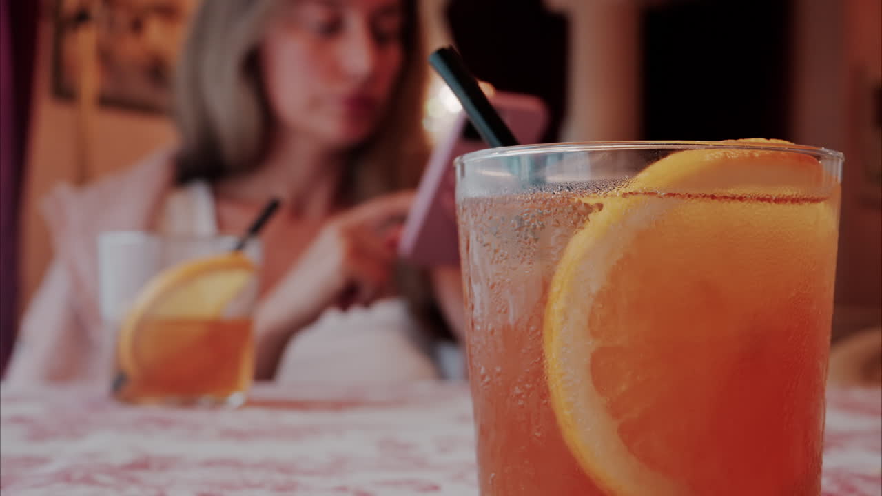Close up of an orange cocktail on a table with a woman on the background at a restaurant