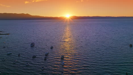 numerous boats sailing on the water of lake tahoe. bright sun setting behind the mountains at backdrop. orange sky at background.