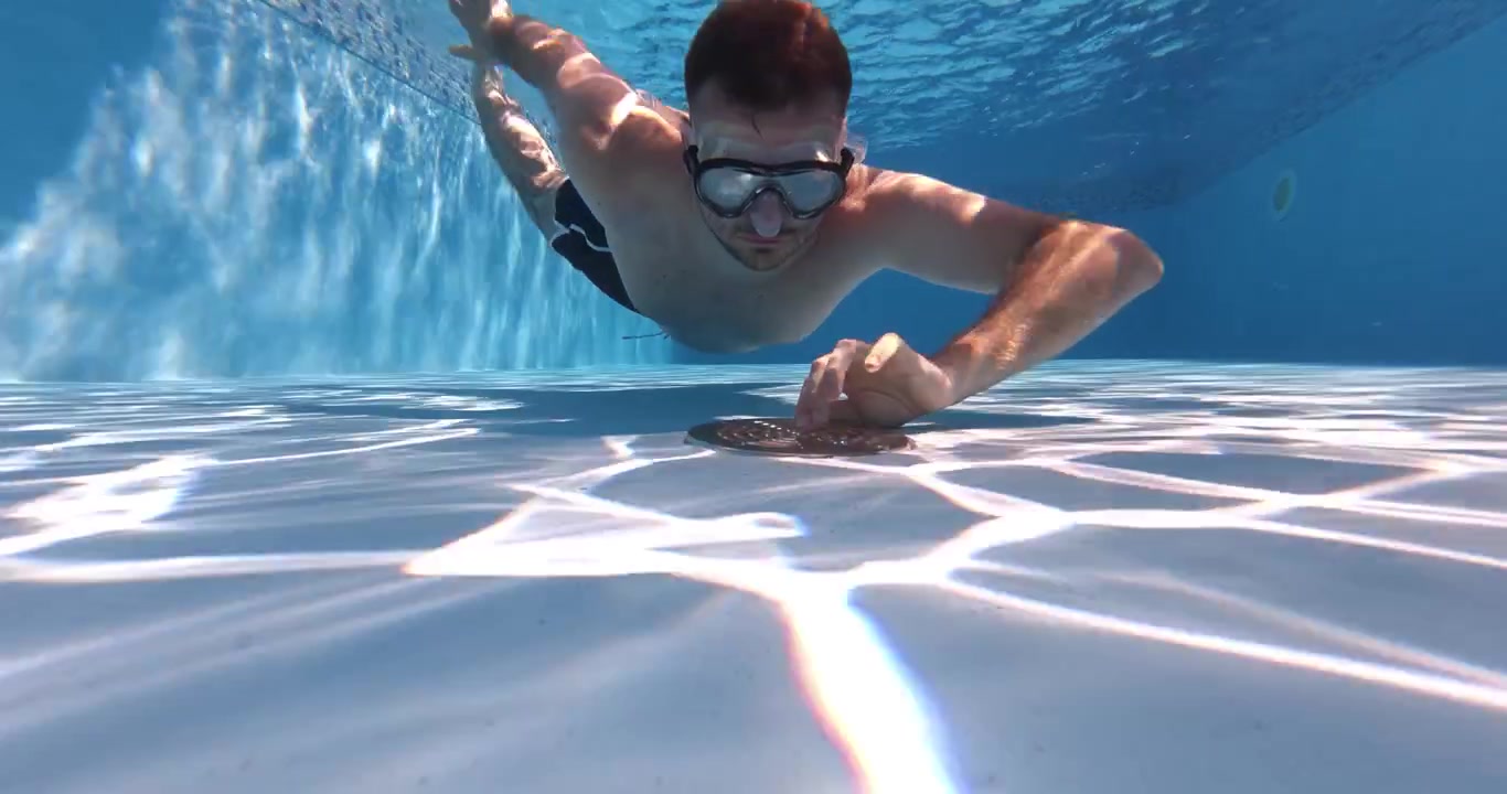 Un uomo che si immerge sott'acqua in una piscina per ispezionare o controllare il sistema di filtraggio della piscina. Focus su manutenzione, ispezione tecnica e servizio subacqueo della piscina.