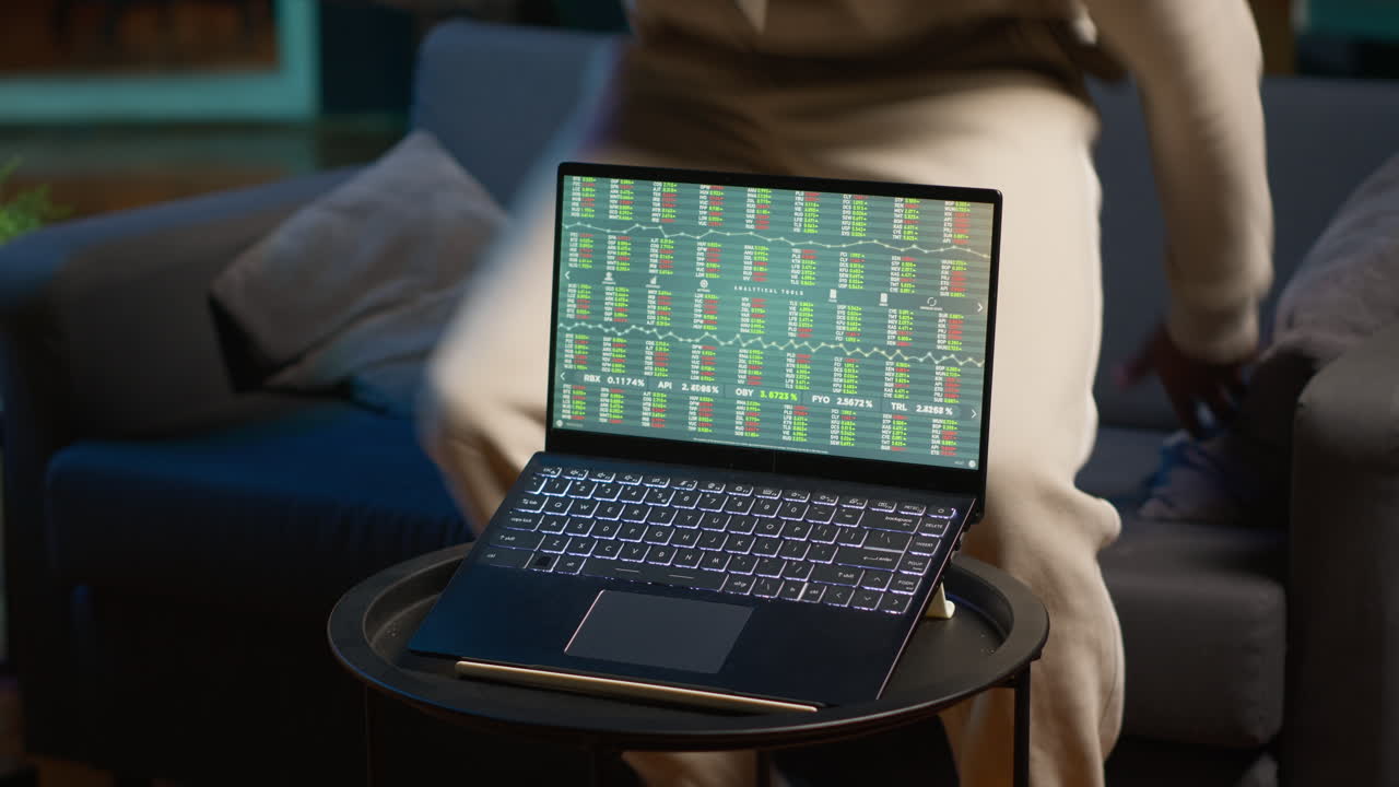 Man enjoying music and reading e books on tablet while waiting for stock market financial figures to get updated on laptop. Person at home next to pc showing trading investment graphs. Camera A.