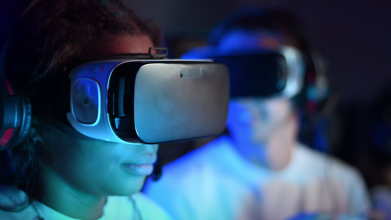 White boy and black girl teens in VR headsets playing video games in video game club with blue illumination using a gamepad. Slow motion