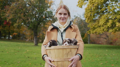 Middle-aged-woman-holding-a-basket-with-small-puppies,-standing-in-the-park-on-an-autumn-day