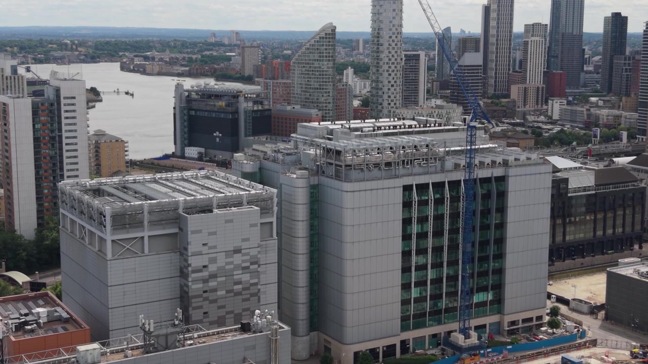 Una prospettiva aerea mostra un moderno edificio di data center a Londra. Lo skyline vibrante della città, con imponenti grattacieli e il tortuoso fiume Tamigi, si estende sotto un cielo diurno luminoso.