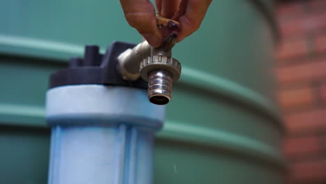 dripping spigot on outdoor water tank turned off by male hand, close up