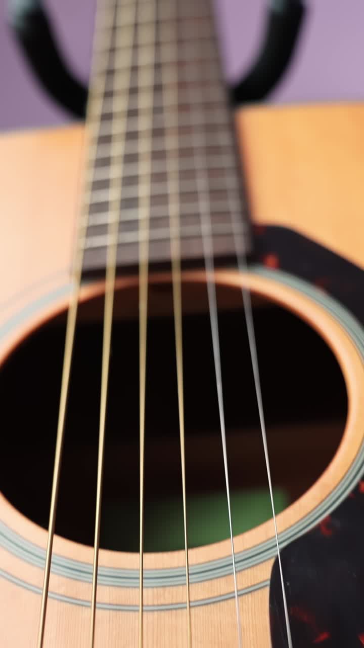 Vertical move down an acoustic guitar neck toward the sound hole on a purple background, with shallow depth of field and copy space for music and studio b-roll