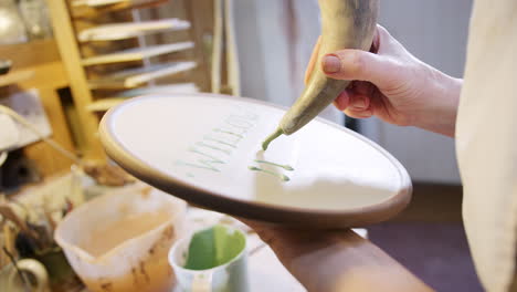 close up of male potter putting lettering onto clay plaque for house sign in ceramics studio