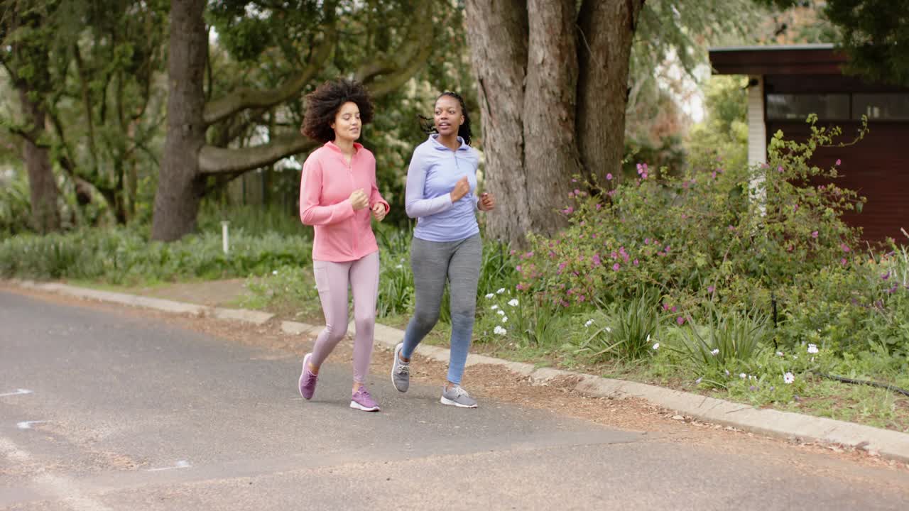 Amiche diverse che chiacchierano mentre fanno jogging lungo una strada suburbana con scarpe da running