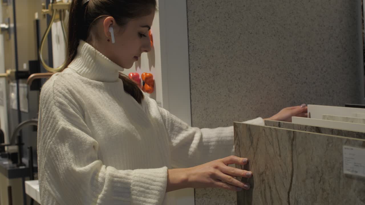 una mujer joven con auriculares inalámbricos blancos elige azulejos