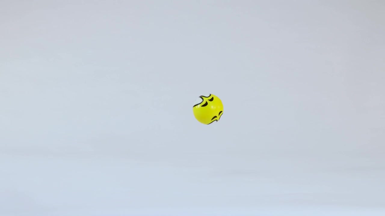 A yellow ball with an emoji face bounces and rolls across a white studio floor