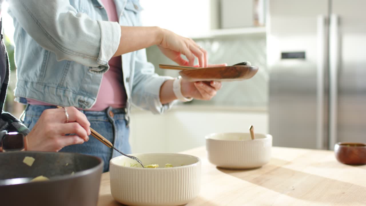 2人の大人がカウンターで、鍋を傾けて調理済みの食べ物をリブ付きのボウルに盛り付けている。
