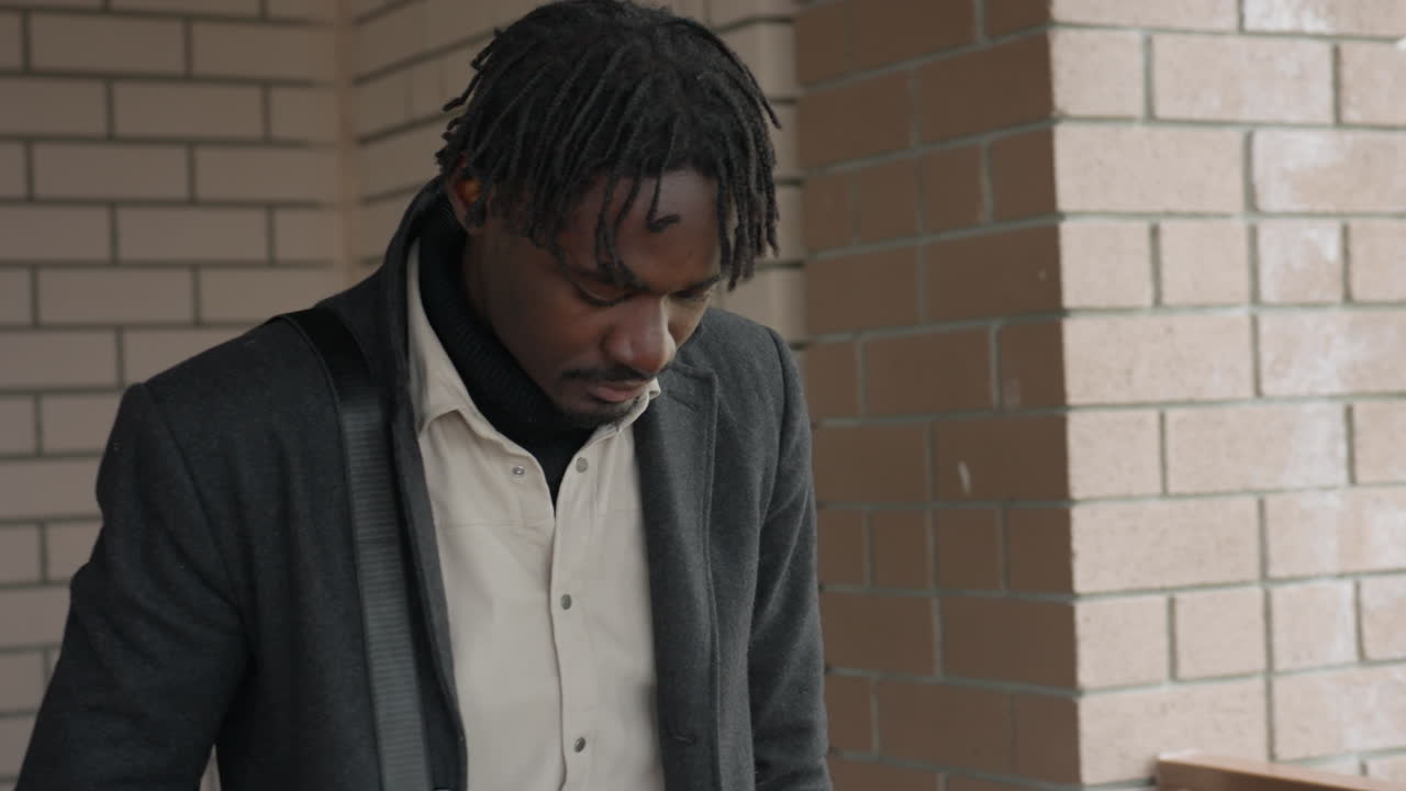 African man with Locs exits hallway, palm to head, worried glance signals delay, urgent stride picks up, time pressure visible on face, movement toward door captures late departure mood indoors