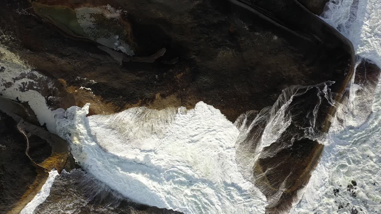 toma de subida suave cenital cinematográfica de olas ásperas del océano golpeando rocas durante la puesta de sol en la playa de la bahía de campamentos de ciudad del cabo
