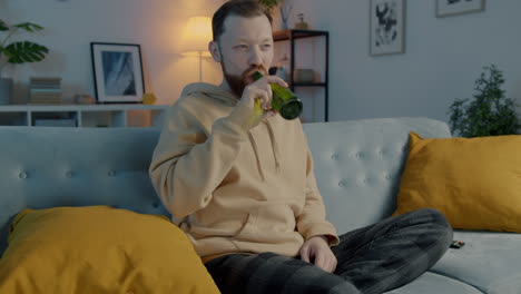 man relaxing on couch with beer and watching tv
