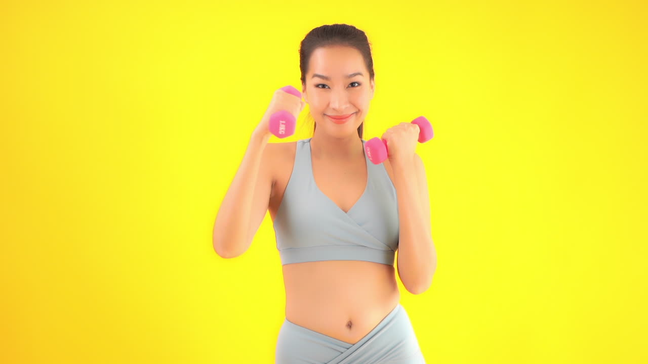 Using small pink dumbells to strengthen her arms, a beautiful woman in athletic wear punches the air