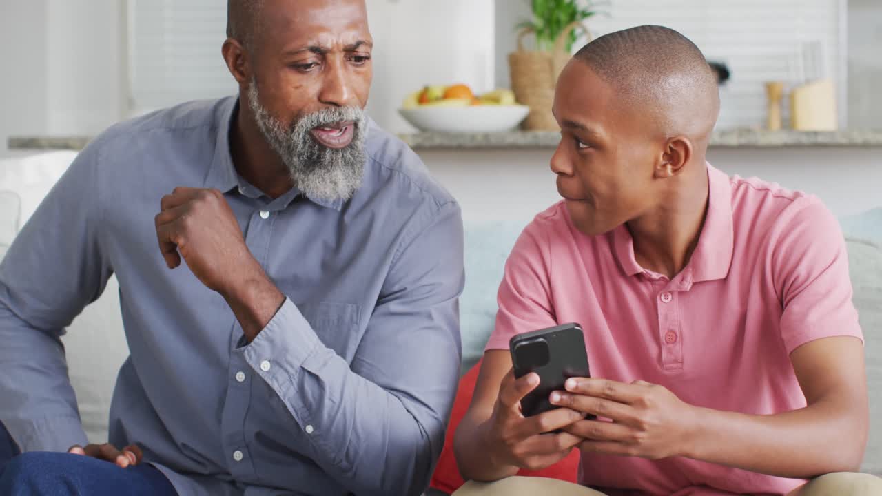 video de un padre y un hijo afroamericanos felices usando un teléfono inteligente juntos