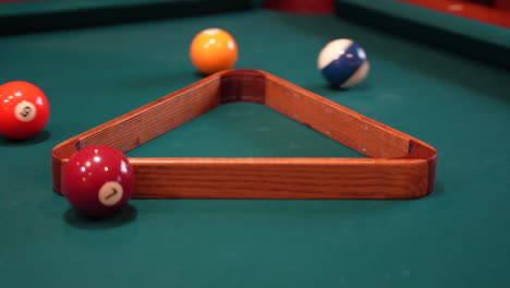 person racks 8 ball pool triangle closeup on the spot then rearranges solid and stripped billiard balls on table with green felt or cloth and tightening rack with hands before lifting wooden triangle