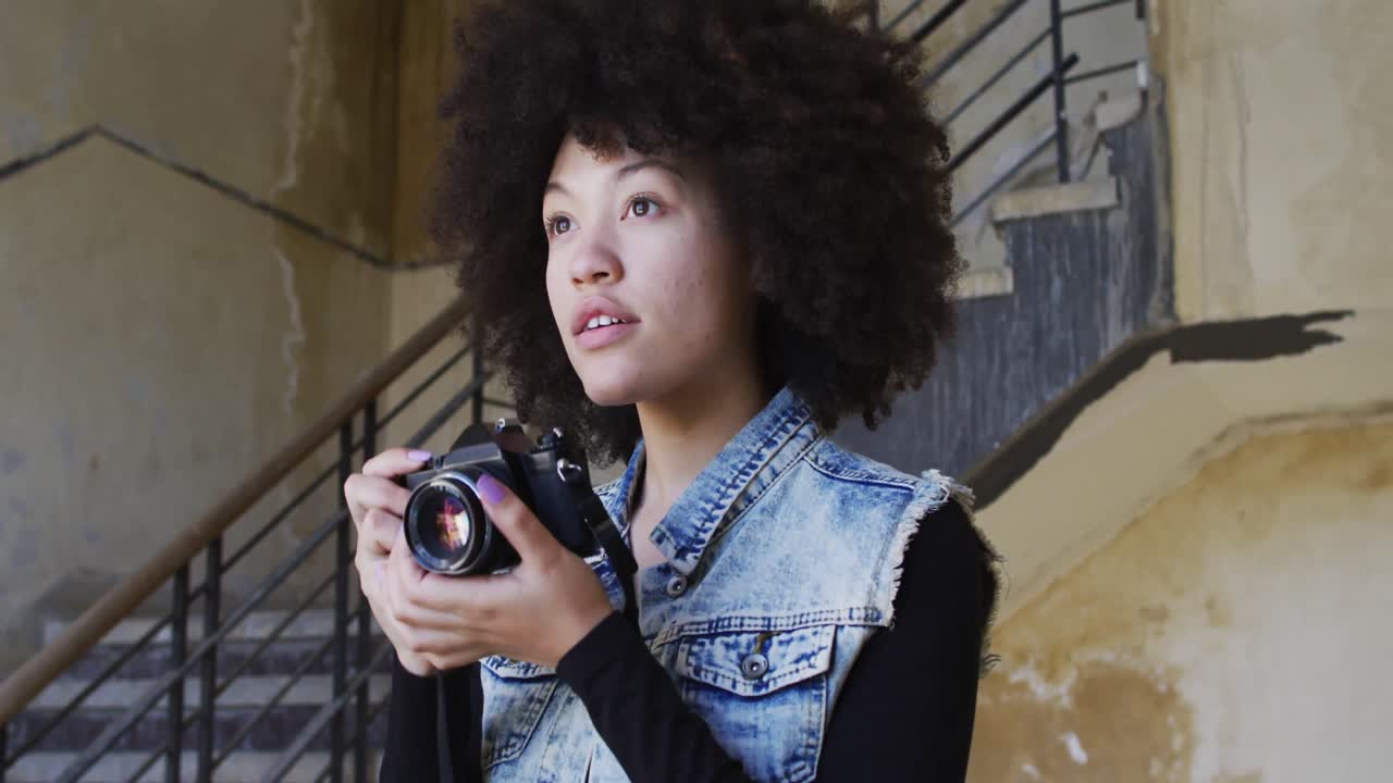 mujer afroamericana tomando fotos con una cámara digital mientras está de pie cerca de las escaleras