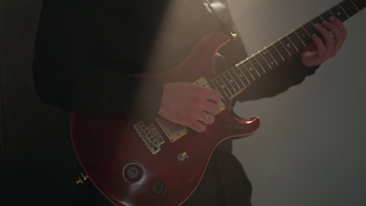 Close-up of a faceless person in black playing a red guitar in a dimly lit room