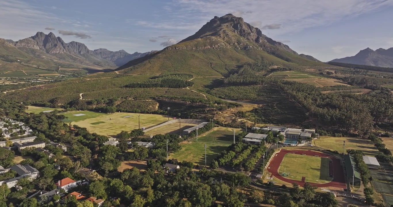 Stellenbosch Südafrika Luftaufnahme v16 Überflug über Wohnbebauung und universitäre Sportplätze unter schroffen Bergen - Aufgenommen mit Mavic 3 Pro Cine - 6. Januar 2024