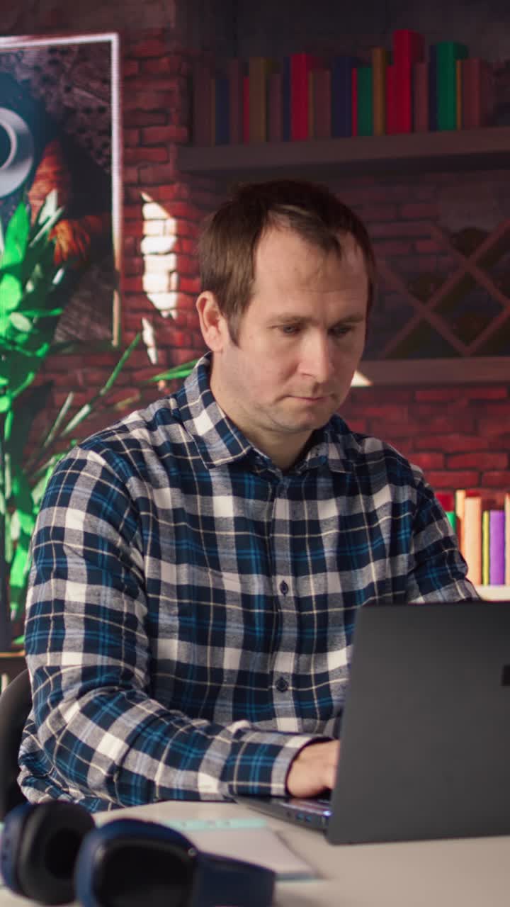 Vertical video Man seated at home office desk using laptop, checking emails