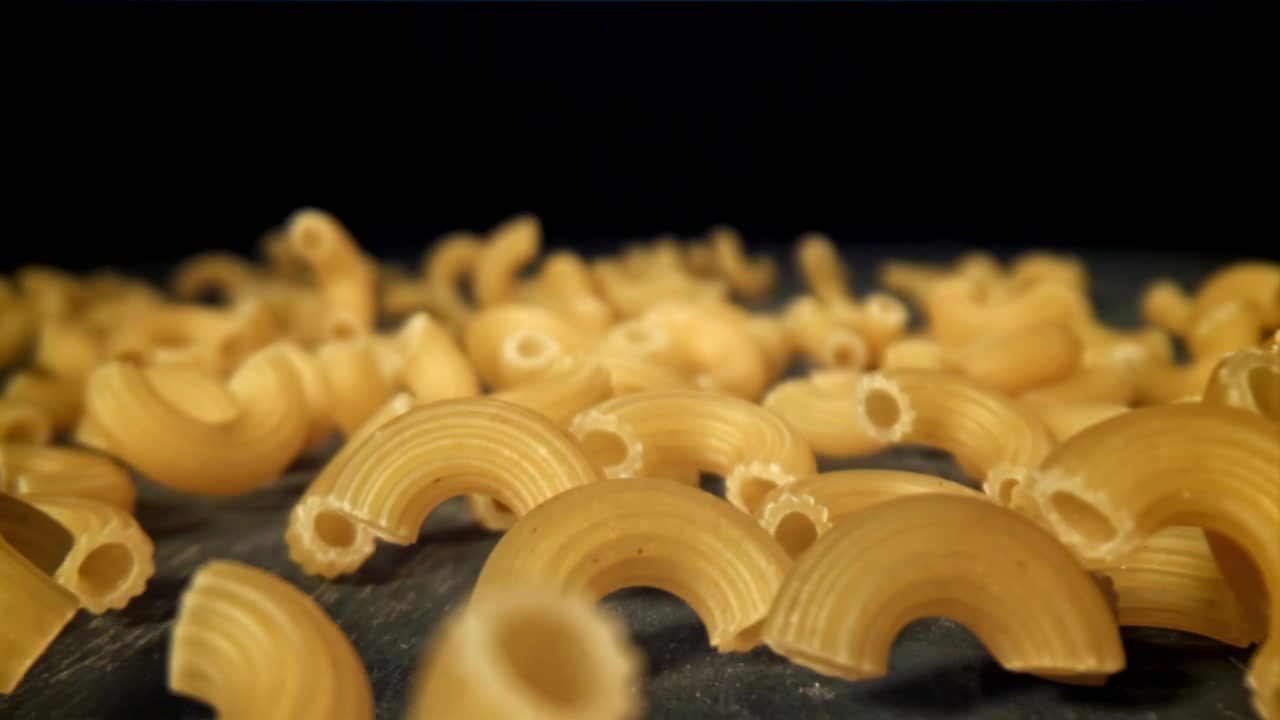Maccheroni secchi che cadono al rallentatore su una superficie scura