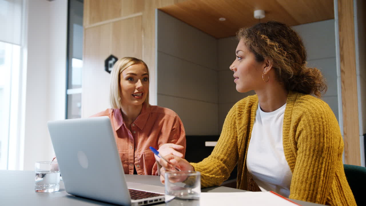 vista de bajo ángulo de dos jóvenes colegas sonrientes sentadas en una oficina trabajando juntas en una computadora portátil, de cerca