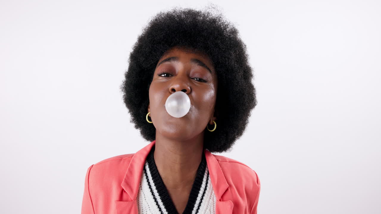 A young woman with an afro blows a bubble gum bubble