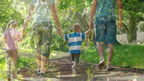 video compuesto de árboles altos contra la vista trasera de una familia caucásica cogida de la mano caminando juntos