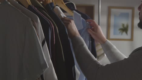 young man at home choosing business suit from clothes rail for job interview