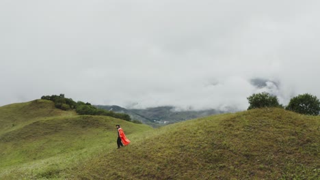 person walking on a mountain path with a red cape