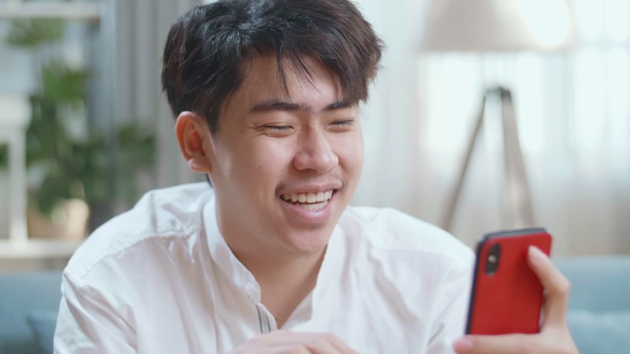 Close Up Of Smiling Asian Man Having Video Call On Smartphone While Sitting On Sofa In The Living Room