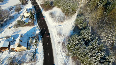 coches que viajan por una carretera asfaltada negra en dirección opuesta entre casas cubiertas de nieve y un bosque invernal cerca de gdansk, polonia