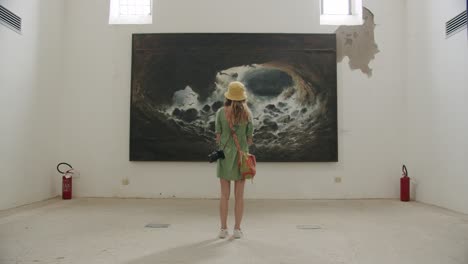 A-young-girl-photographer-is-looking-at-a-big-painting-in-the-musuem-of-the-Certosa-di-San-Giacomo-in-Capri,-in-Italy