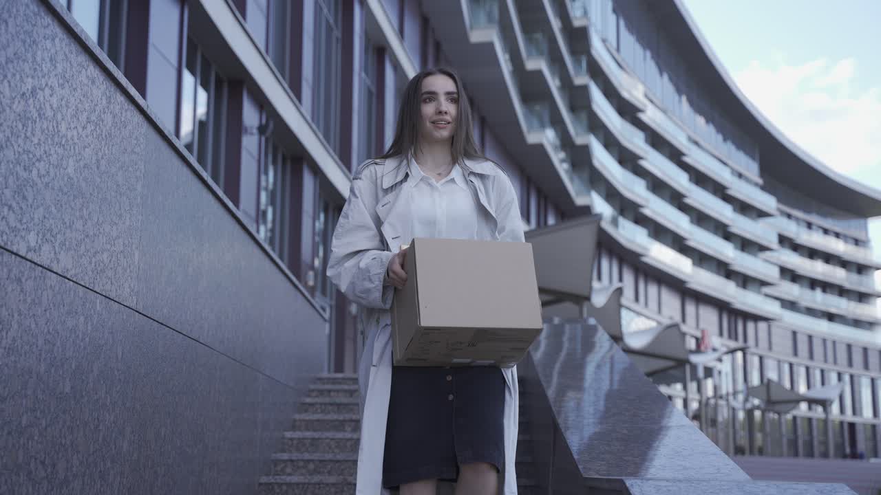 예쁜 여자가 막 직장을 그만뒀어요. 그녀는 사무실 건물에서 나오고 있다. 그녀는 행복하다. 그녀는 웃고 있다.