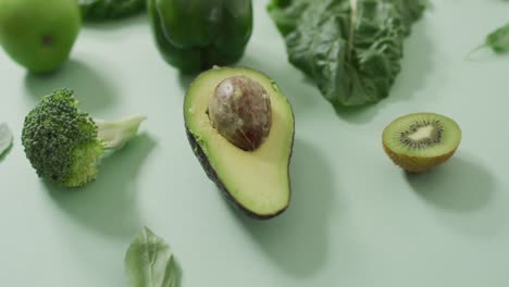 Video-of-fresh-avocado,-broccoli,-green-pepper,-apple-and-green-leaves-on-green-background