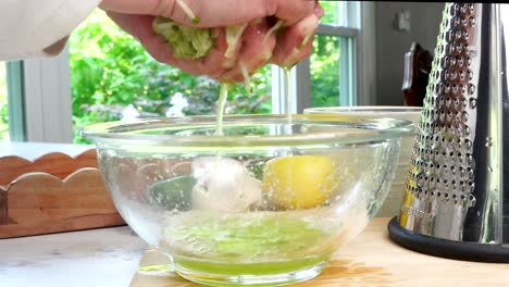 squeezing water out of cucumbers. making tzatziki greek or mediterranean sauce or dip for a party. dip or sauce in a green bowl on a wooden cutting board with dill, green napkin and a grater.