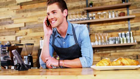 Male-waiter-talking-on-mobile-phone-at-counter